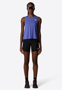 Top deportivo sin mangas morado y pantalones cortos negros, con un logo en el pecho y en los pantalones cortos, acompañados de zapatos negros y rojos.