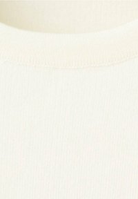 Gros plan d'un tissu tricoté blanc cassé avec une fine texture côtelée et un col rond.