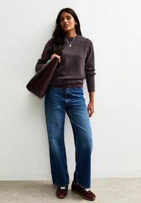 Donkergrijze gebreide trui met lange mouwen, blauwe wijde jeans en een bordeauxrode handtas; ook voorzien van donkerrode sneakers met witte veters.
