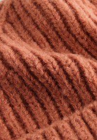 Tissu en maille côtelée dans une couleur terracotta chaude, présentant une texture douce et un motif épais avec des sections en relief bien marquées.