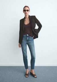 Mörkbrun skräddarsydd kavaj över en brun linne, kombinerad med ljusblå tajta jeans och mörkbruna kilklackar; minimalistisk design.