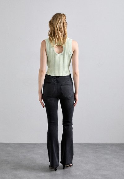 Light green ribbed sleeveless top with a back cutout, paired with fitted black flared jeans. The outfit features a smooth texture and clean lines.