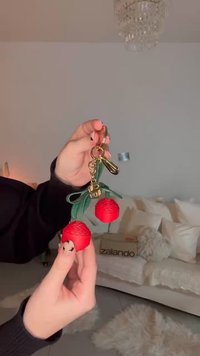 Keychain featuring red rubber cherry design with green leaf accents, attached to a gold metal clip, held in a hand.