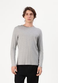 Langærmet grå bomulds t-shirt med rund hals. Enkel design, let stof og en afslappet pasform. Bæres med sorte bukser.