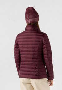 Chaqueta acolchada color burdeos con segmentos acolchados horizontales, cuello alto y un gorro de punto suave a juego.