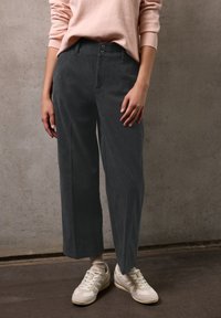 Pantaloni di velluto a coste grigi con una forma dritta, due bottoni in vita e un motivo a coste verticali testurizzato. Indossati con sneaker chiare.