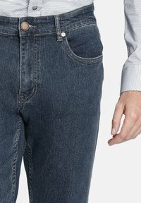 Vaqueros de mezclilla azul oscuro con un diseño clásico de cinco bolsillos, que cuentan con una cinturilla resistente, remaches de cobre y un ligero desgaste.