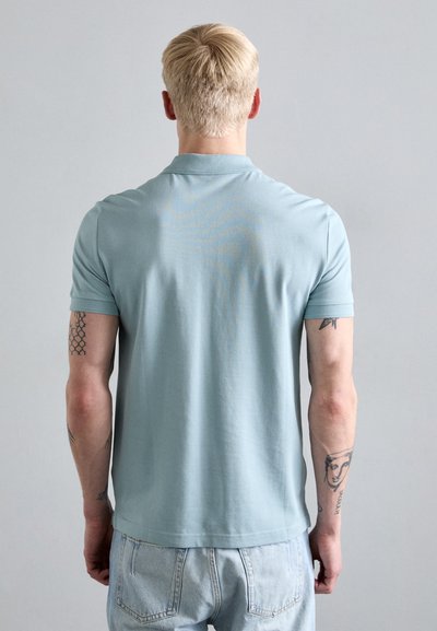 Svetlo modra polo majica iz mehkega blaga, ki ima klasičen ovratnik in kratke rokave. Zadašnji pogled prikazuje sproščen kroj in gladko teksturo.