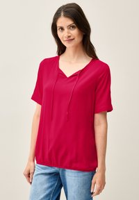Top a maniche corte con scollo a V di un vivace rosso, dotato di un dettaglio con cordoncino. Tessuto morbido e leggero con una vestibilità ampia e una texture liscia.