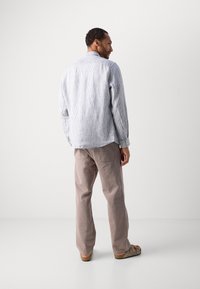 Striped blue and white long-sleeve shirt, paired with light brown pants and sandals, viewed from the back. Casual fit, relaxed design.