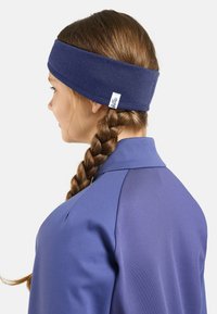 Navy Stoffhaarband, weich und breit, getragen zu einem geflochtenen Haarschnitt, kombiniert mit einer passenden blauen Jacke mit Kragen und Nahtdetails.