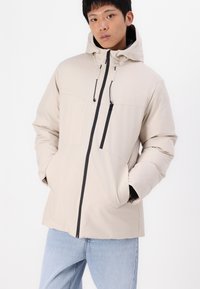 Beige isolierte Jacke mit Kapuze, Fronttaschen und einem durchgehenden Reißverschluss. Mit schwarzen Akzenten und einer glatten, matten Textur.