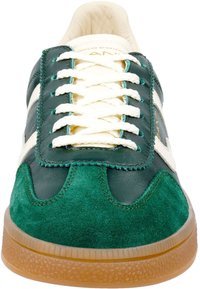 Green leather and suede sneaker with white stripes, round toe, textured rubber sole, and contrasting tan outsole. Features lace-up design.