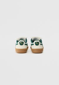 Weiße und grüne Sneakers mit Gummisohlen, gepolstertem Kragen, Klettverschlüssen und einem goldenen Logopunkt auf der Ferse und den Seiten.