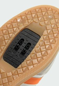 Podeszwa buta z jasnobrązowej gumy, teksturowanym wzorem diamentowym, czarnym obszarem na korki oraz pomarańczowymi i białymi detalami w górnej części.