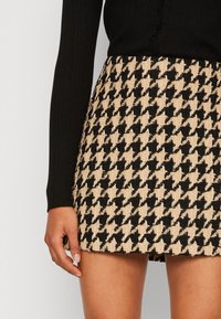 Mini sukně s černo-beige houndstooth vzorem vyrobená z texturované látky, s rovnou siluetou a páskem.
