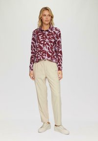 Lange mouwen shirt in bordeauxrood met een bloemenpatroon in lavendel, gecombineerd met beige broek met zijzakken en witte sneakers.