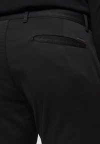 Zwarte broek met een gladde textuur. Kenmerkend zijn de slim fit, een achterzak met een subtiele afwerking en een naadloze tailleband.