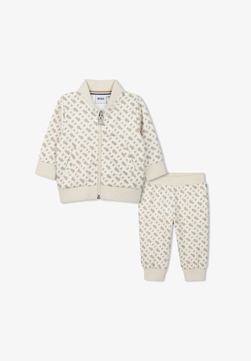 Ensemble beige à deux pièces comprenant une veste bomber zippée et un pantalon assorti. Présente un motif géométrique marron clair. Tissu doux, poignets et taille côtelés.