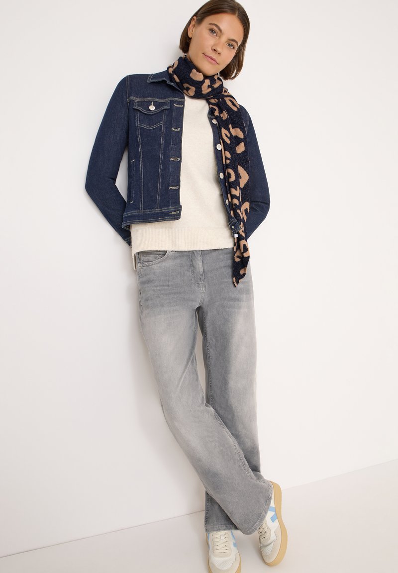 Mørkeblå denimjakke, hvid sweater, lysegrå jeans og et tørklæde med leopardprint. Sneakers i lysegrå med blå detaljer og beige såler.