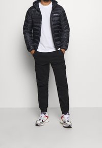 Czarna kurtka puchowa z kapturem, biała koszulka, czarne spodnie cargo i wielokolorowe trampki, z elastycznymi mankietami i bocznymi kieszeniami.