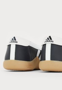 Black leather athletic shoes with a white rubber trim and three black stripes. The sole is tan rubber, providing contrasting color and texture.
