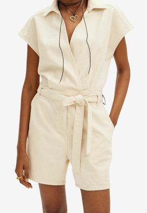 Beige denim jumpsuit met een kraag, korte mouwen en een strikceintuur in de taille. Heeft een ontspannen pasvorm en voorzakken voor praktisch gebruik.