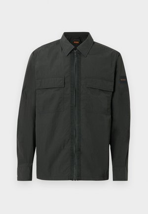 Zwarte lichtgewicht jas met een ritssluiting aan de voorkant, twee borstzakken en een subtiel logo op de mouw. Voorzien van een gestructureerde kraag en lange mouwen.