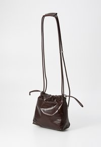 Dark brown leather drawstring crossbody bag with long adjustable strap and gathered top detail on a plain background.