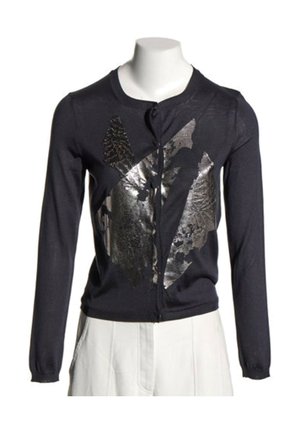 Cardigan noir à manches longues boutonné avec motif abstrait de feuille argentée brillante, porté avec un pantalon blanc sur un mannequin sans tête.