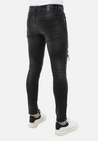 Zwarte denim jeans met een slim fit, voorzien van een versleten look op de benen, en gecombineerd met witte sneakers met zwarte accenten.