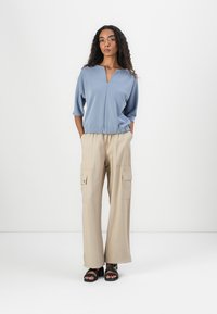 T-shirt azul claro com decote em V e mangas de 3/4, combinada com calças cargo bege com bolsos laterais. Usada com sandálias pretas.