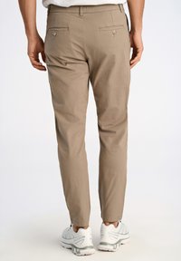 Lichtbruine chinos met een slim fit, twee achterzakken met knopen en een elastische tailleband. Gepaard met witte hardloopschoenen.