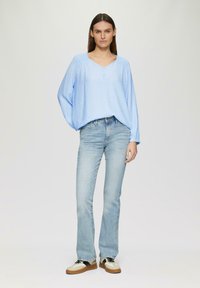 Haut bleu clair à manches longues en tissu texturé avec un décolleté en V et des détails de boutons, associé à un jean bleu clair évasé et des baskets bicolores.