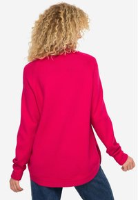 Maglione magenta con maniche lunghe, polsini a coste e una vestibilità leggermente oversize. Presenta spacchi laterali e una texture liscia.