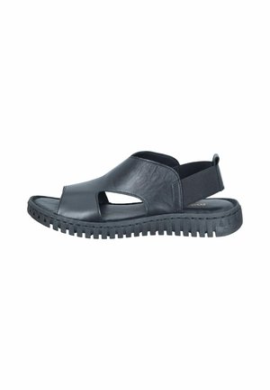 Black leather open-toe sandal with cut-out sides and elastic back strap on a rugged, textured sole against a white background.