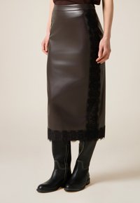 Gonna in pelle nera con bordatura in pizzo all'orlo, design elegante, silhouette dritta, abbinata a stivali neri al ginocchio con cuciture bianche.