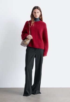 Red fluffy sweater paired with wide-leg black pants. Model holds a small, patterned bag. Simple background enhances focus on outfit.