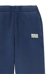 Tumši zili sporta bikses ar teksturētu audumu, elastīgu jostasvietu, sānu kabatām un baltu "AMERICAN VINTAGE" logotipu priekšpusē.