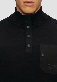 Schwarzer Strickpullover mit hohem Kragen, ausgestattet mit vier schwarzen Knöpfen und einer Tasche mit Logodetail auf der linken Brust. Strukturiertes Material.
