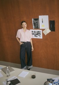 Light pink short-sleeve shirt with ruffled neckline, paired with dark wide-leg jeans featuring a cuffed hem. Brown wood background.
