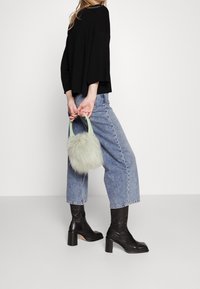 Czarna, oversize'owa bluzka, jasnoniebieskie, krótkie jeansy, czarne kozaki na obcasie i futrzana torebka w miętowym kolorze z krótkimi uchwytami.