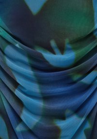 Tissu transparent présentant un dégradé de tons bleu profond et vert, avec un drapé doux et texturé ainsi que des motifs abstraits sur toute la surface.