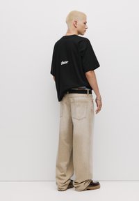 Sort oversized t-shirt med hvidt logo på ryggen, suppleret med lysebeige baggy jeans og mørkebrune sko. Glat stof, afslappet pasform.