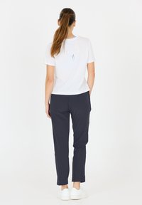 Vit kortärmad t-shirt med en utskärning på baksidan, kombinerad med mörkblå avsmalnande byxor och vita sneakers. Enkel, strömlinjeformad design.