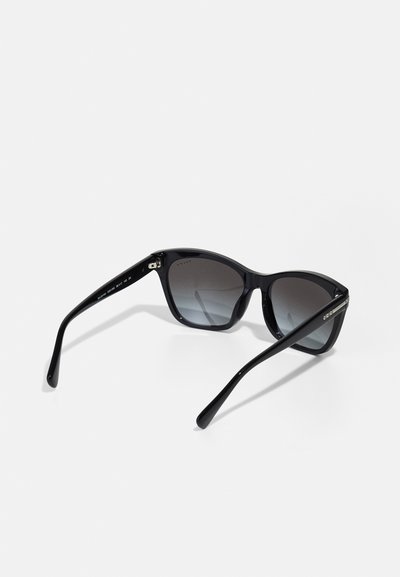 Ochelari de soare cu formă de pisică, cu ramă din plastic negru, lentile gri cu gradient și brațe subțiri negre cu accente metalice.