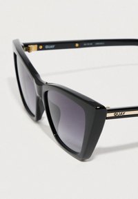 Czarne plastikowe okulary przeciwsłoneczne o wyrazistym kocim kształcie. Soczewki z gradientem szarości, złote akcenty na zausznikach oraz logo na boku.