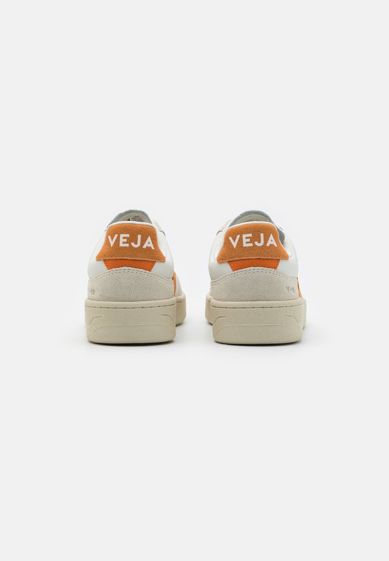 Baskets en cuir blanc avec des accents en daim orange et le logo "VEJA" sur le talon, présentant une semelle en caoutchouc beige texturée et un design simple.