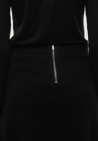 Vêtement noir avec une texture lisse, des manches longues et un détail de fermeture éclair argenté à l'arrière, créant un look épuré et moderne.