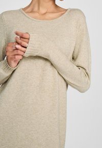 Maglione beige a maglia con scollatura ampia e polsini a costine, caratterizzato da una texture morbida e una vestibilità rilassata.